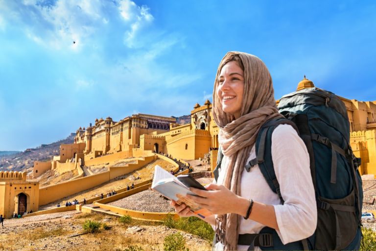 A solo female traveler smiles while holding a guidebook outside Amber Fort in Rajasthan.
